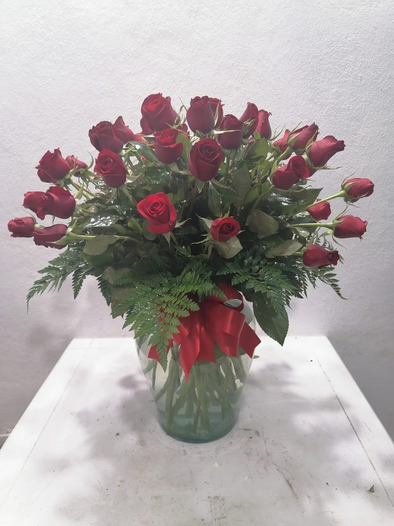 Rosas rojas y hojas verdes en original florero de cristal